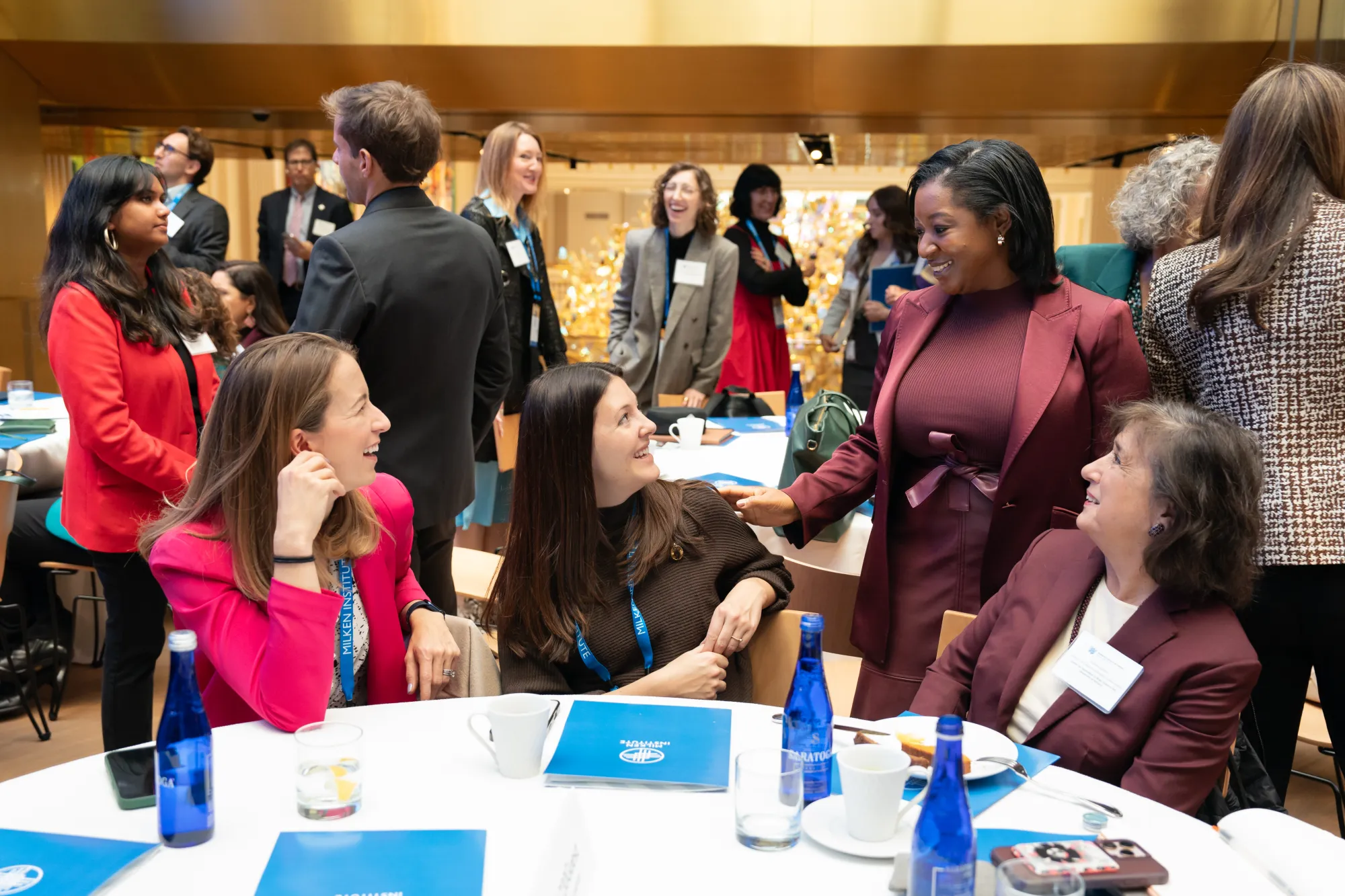 Attendees networking and conversing at a Milken Institute Women's Health event, with Milken Institute-branded materials on the tables.