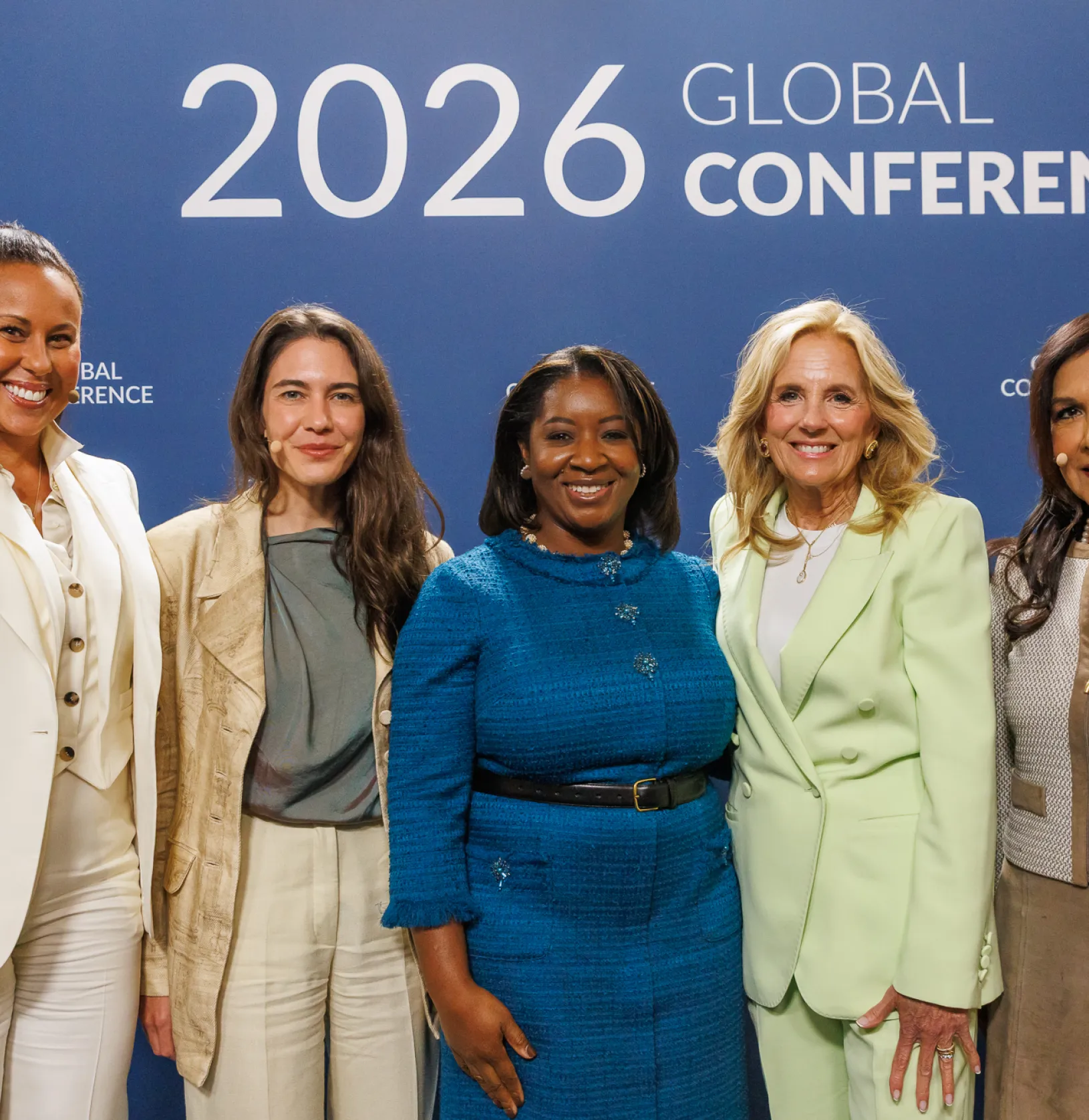 Five women pose together smiling at the 2026 Milken Institute Global Conference, standing in front of a blue backdrop with the conference logo.